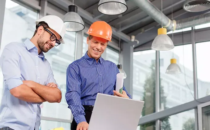 Two men in hard hats looking at a laptop